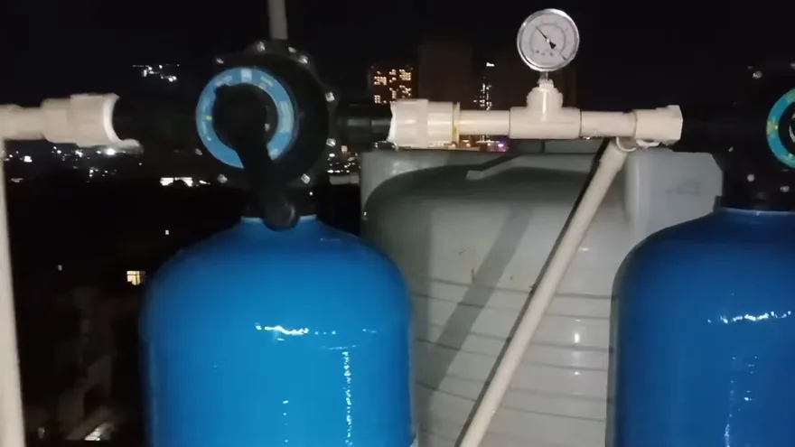 Two blue filter tanks joined by white piping with a round pressure gauge on top, photographed at night