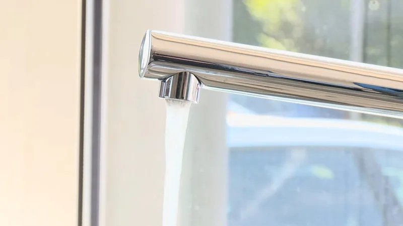 Water running from a chrome faucet spout in bright light beside a window