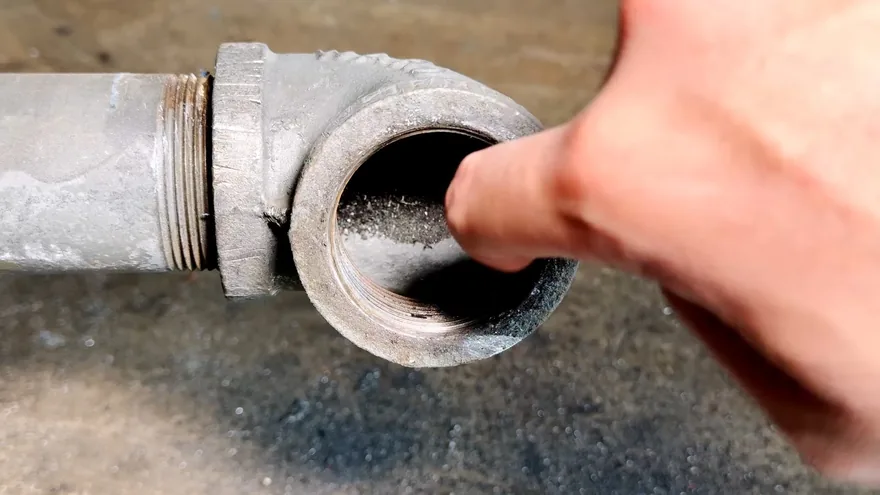A finger resting in the open threaded end of a galvanized pipe elbow
