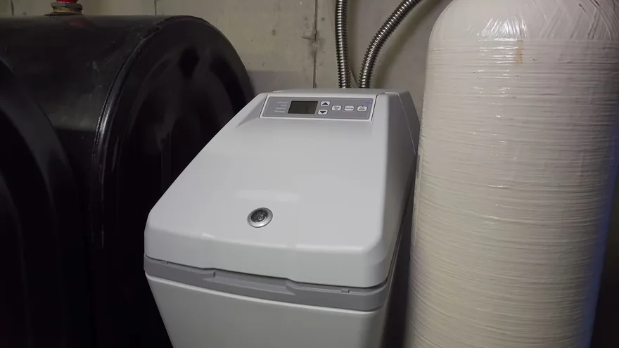A gray water softener cabinet beside a black brine tank and a white resin tank against a wall