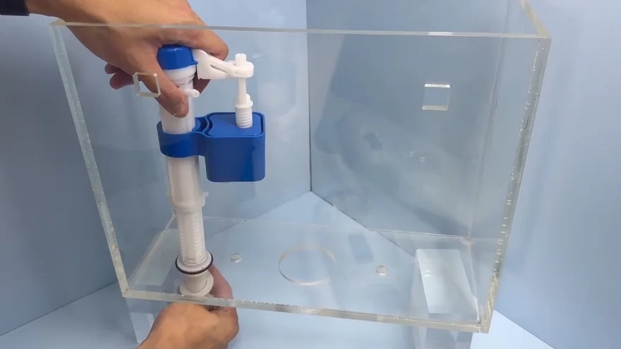 A hand holding a blue and white fill valve upright inside a clear toilet tank