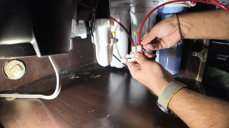 Two hands joining the wires of a disposal in a dark sink cabinet beside a white trap