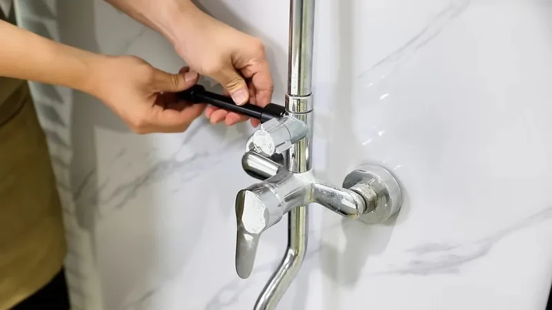 Hands removing the handle from a chrome shower valve set in a white marble-look wall