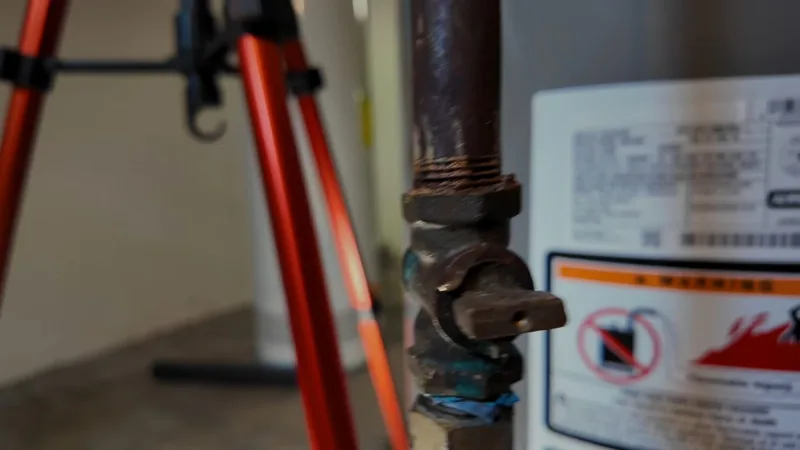 A rust-brown iron gas shutoff valve beside a water heater with a warning label