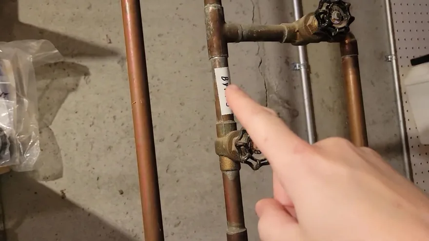 A finger pointing at a valve on copper supply pipes against a concrete wall
