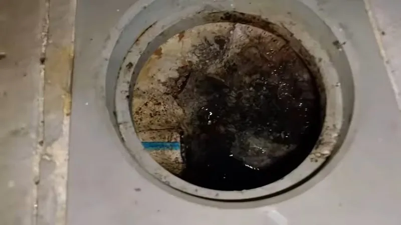 A round floor drain opening filled with dark water and debris