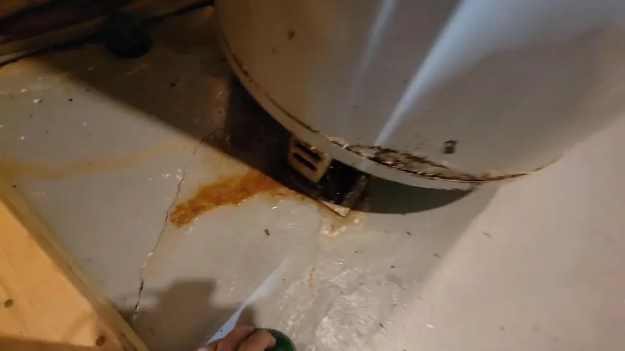 A rust-colored stain on a cracked concrete floor beside the base of a water heater