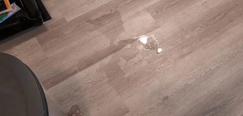 Water spreading across a wood-look plank floor with a bright reflection at one edge