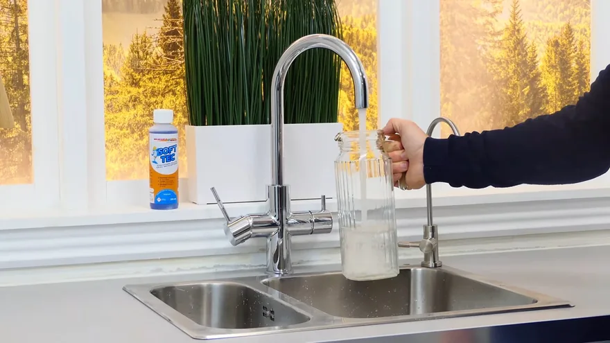 A hand holding a glass jar under a chrome kitchen tap with a double sink below