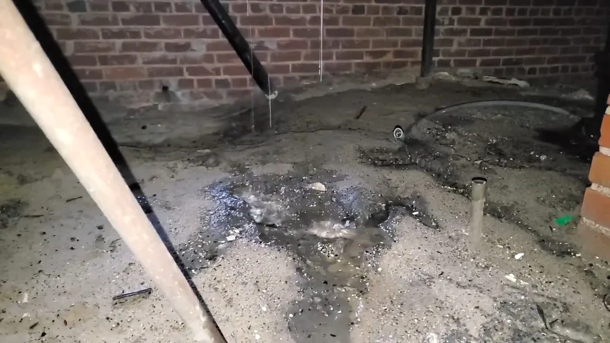 Dark wet sludge and standing water spread across a crawl space floor beside a brick wall